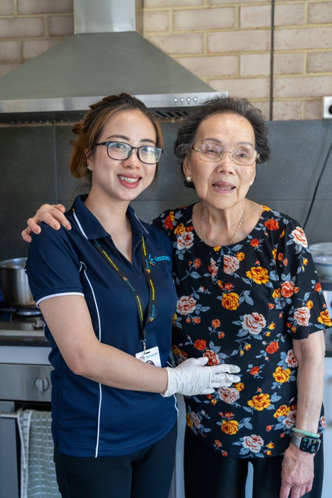 A happy older woman embracing a smiling staff person. Both are from multicultural backgrounds.