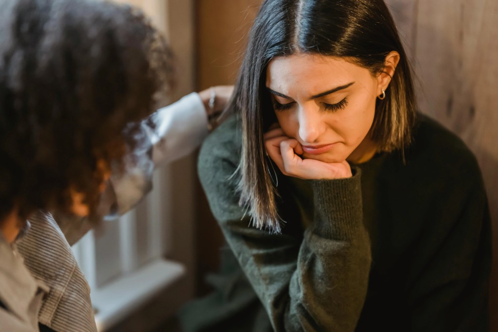 A young woman feeling sad is being comforted and supported by another woman