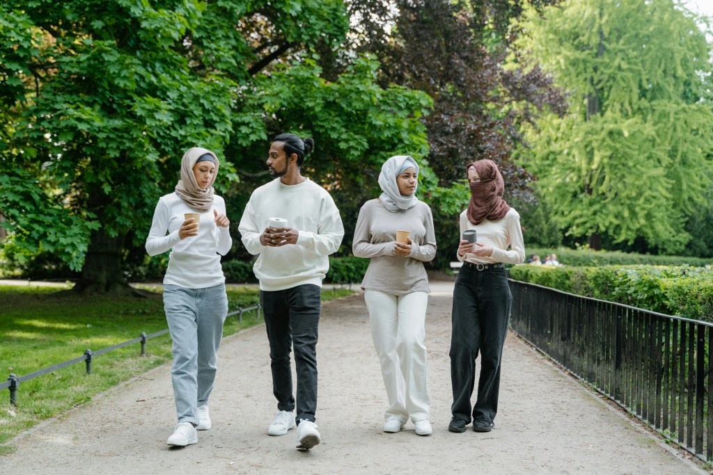 A group of diverse young friends socialising and going for a walk together in a park with coffee.