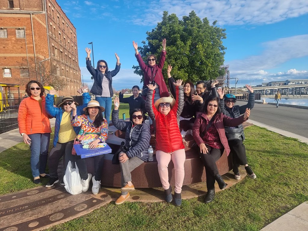 A women's social group on an outing, smiling and raising their hands up!