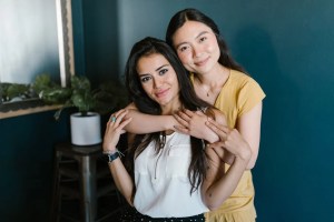 Two women from multicultural backgrounds smiling and hugging one another.